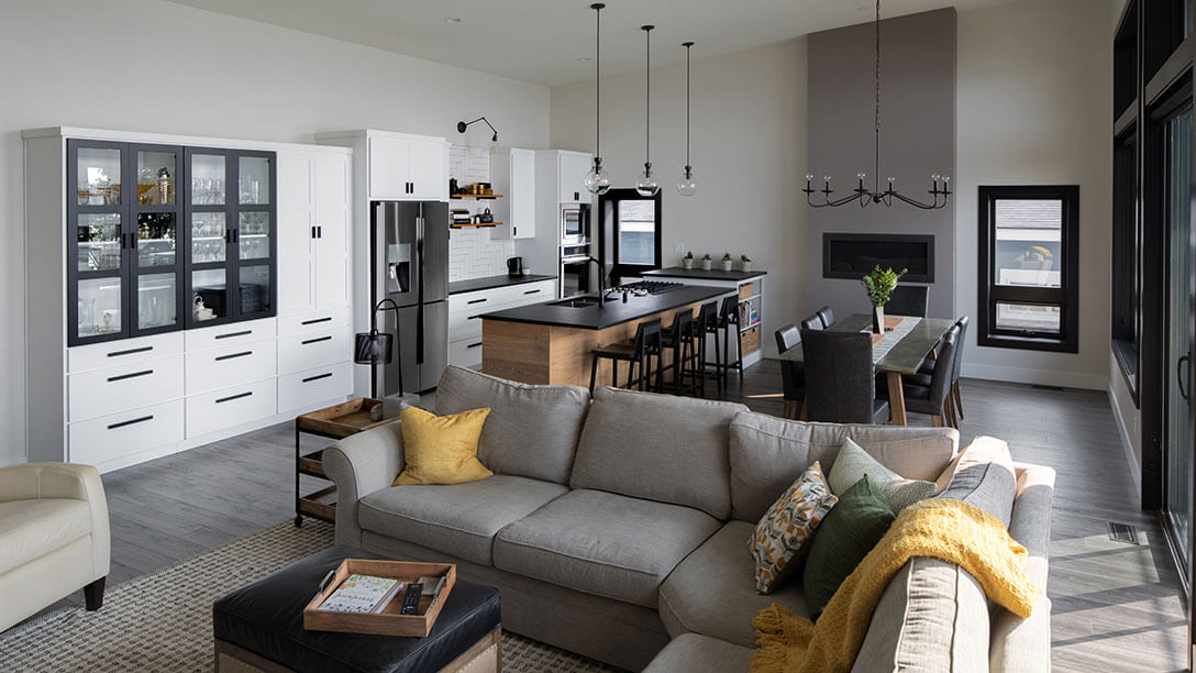 An open concept living room and kitchen with white cabinets, wood flooring and black accents.