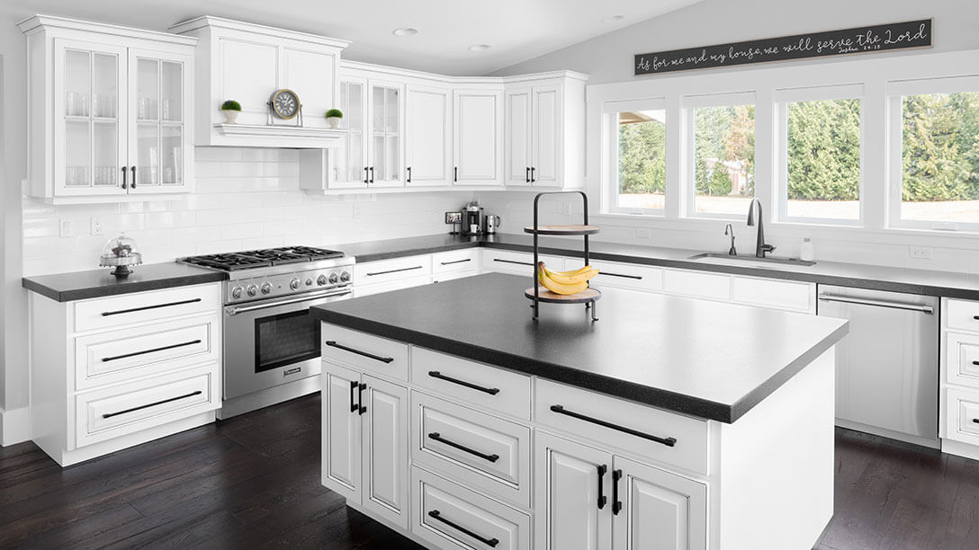 A white modern farmhouse kitchen with stainless steel appliances, wood flooring and black granite countertops.