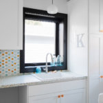 White cabinets, orange knobs, and custom black windows in a bright laundry room.