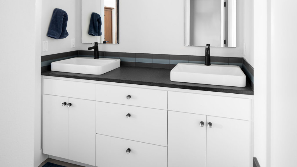 A white European style cabinet vanity with black granite countertops in a master bathroom.