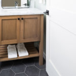A powder bathroom with gray hexagon floor tile, a wood cabinet vanity and marble countertop.