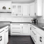 A modern white farmhouse kitchen with white cabinets, stainless steel appliances and black granite countertops.