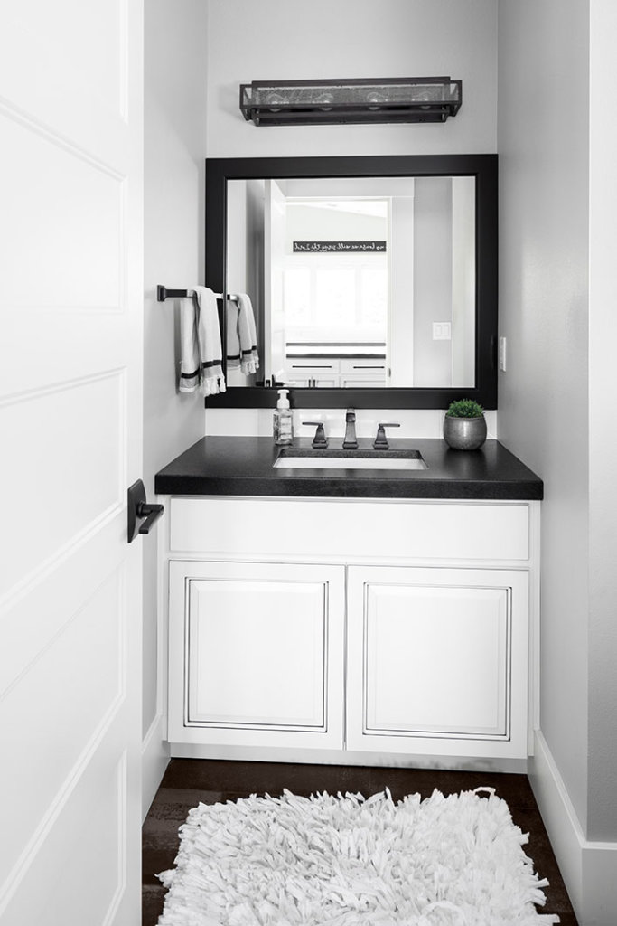 A farmhouse style bathroom with white cabinet vanity, black finishes, and black granite countertop.